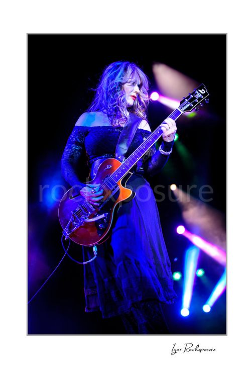 Vertical color image of Nancy Wilson performing with electric guitar during a Heart concert under vivid purple and blue stage lights