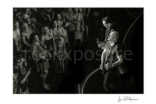 Horizontal black and white image of Vivian Campbell and Phil Collen of Def Leppard performing live on stage, viewed from above with audience members surrounding the stage