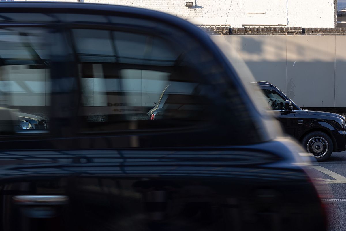 Suddig svart London-taxi som passerar i stadstrafik, etableringsbild i en redaktionell bildber&auml;ttelse.