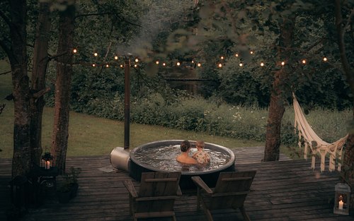 Outdoor fire pit area surrounded by trees near a black cabin