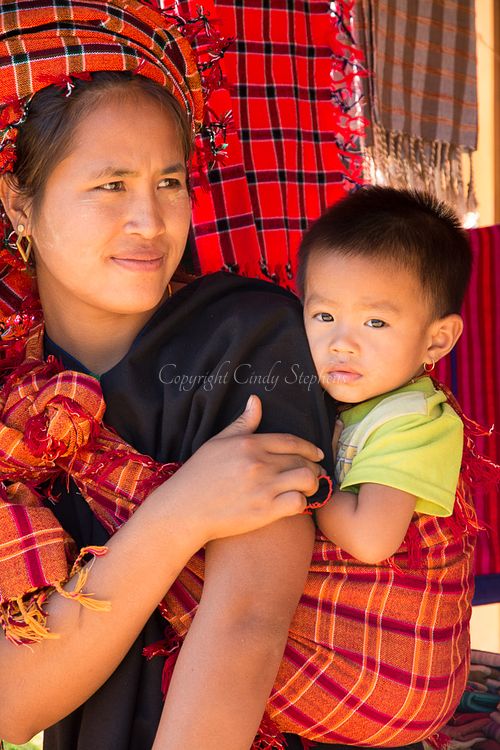 Mother holding her baby, both dressed in colorful red traditional clothing, representing the vibrant culture of Myanmar