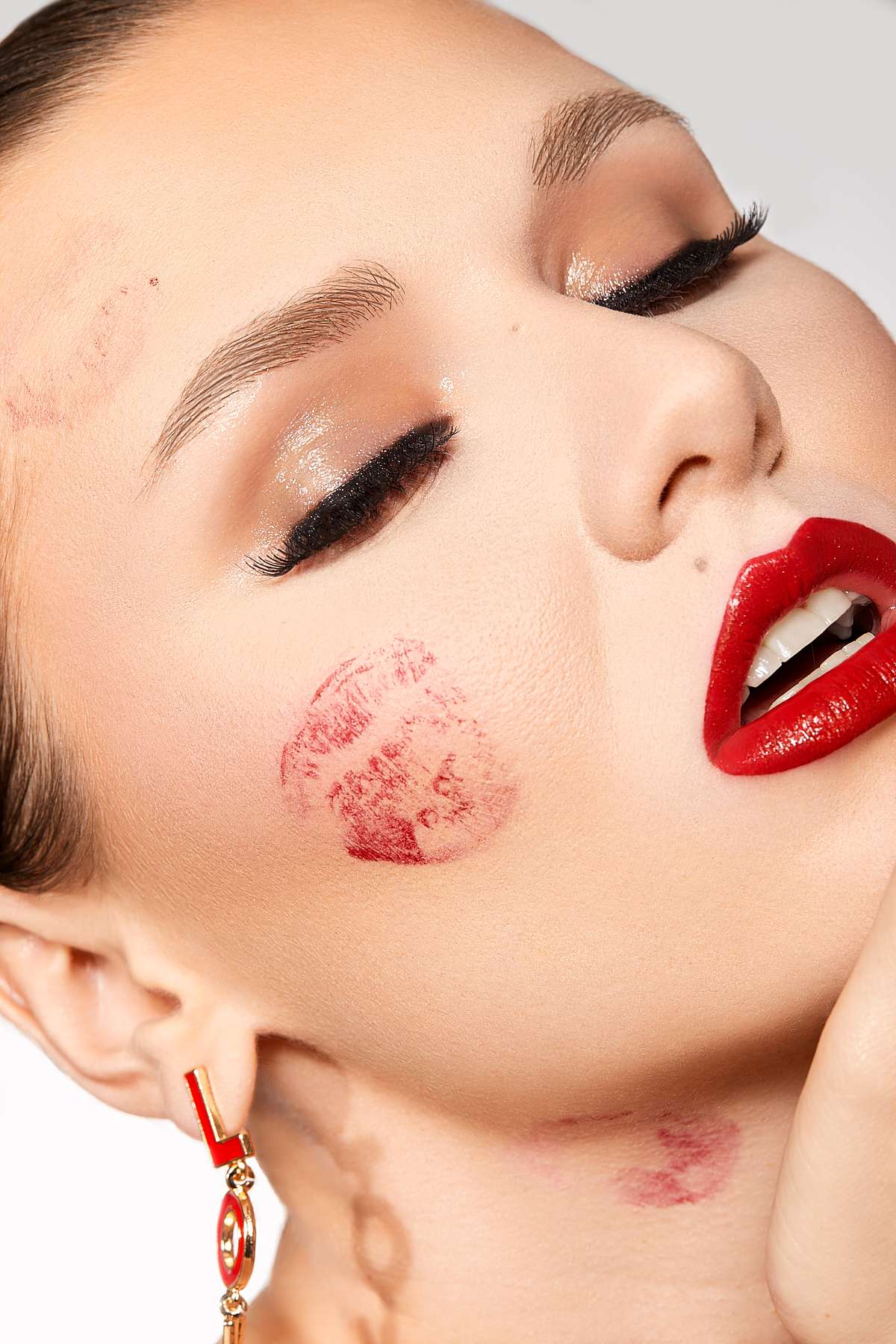 Close-up of a woman's face with bright red lipstick marks on her cheek and neck.