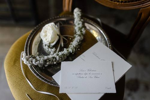 Invito di matrimonio e accessori disposti su un tavolo illuminato da luce calda.