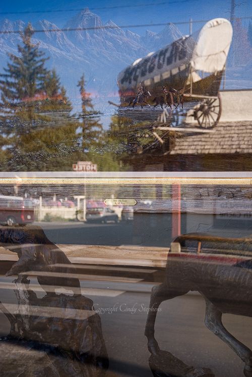 Reflections of a stagecoach and horseback riders in a main street scene with mountains and western sculptures