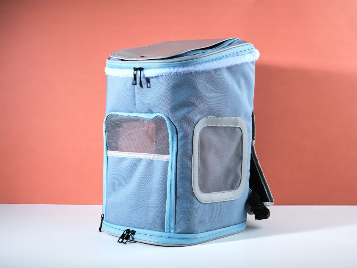 Blue KibbleTime backpack pet carrier on a salmon and white background.