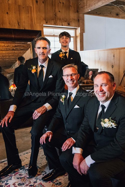 A groom and three groomsmen dressed in tuxes sitting on a couch