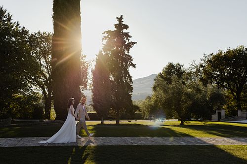 Gli sposi che camminano in mezzo al giardino della tenuta santi giacomo e filippo con il sole che filtra attraverso gli alberi
