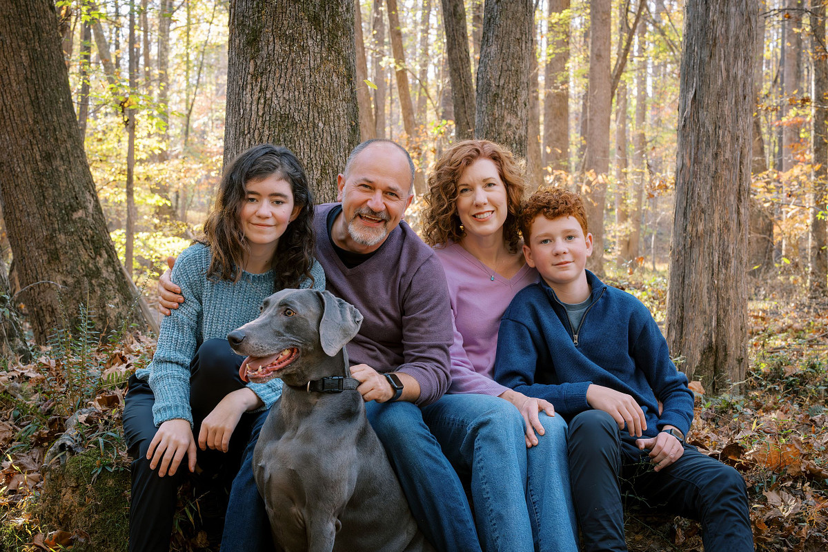 A family posing for a portrait with their dog in Carolina North Forest in Carrboro, NC