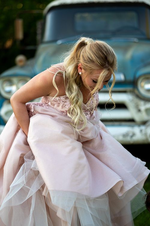 High School Grad gathering her pink gown in front of a vintage blue truck.