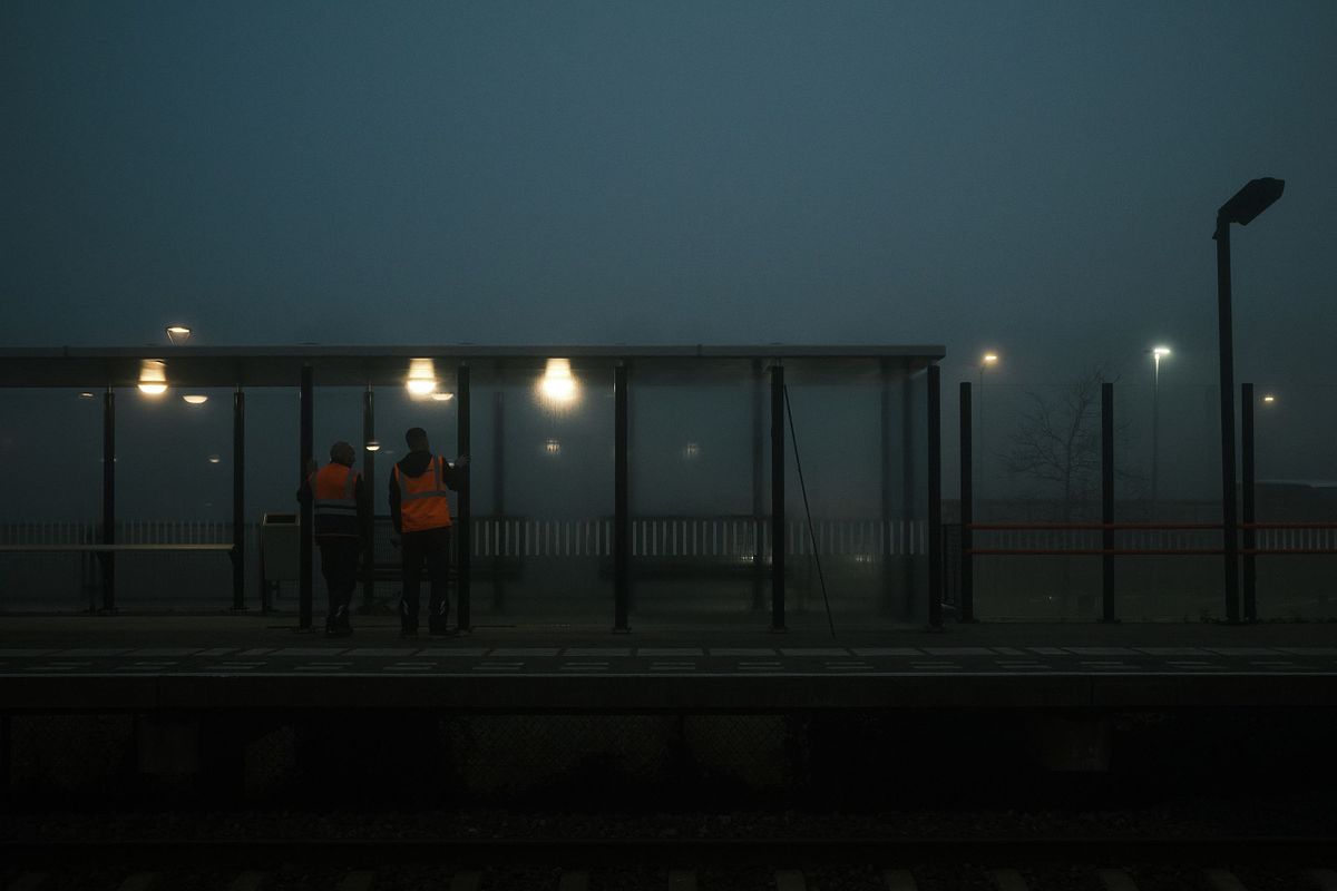 Two people in orange vests at a foggy train station, captured by photographer Sandeep Gajula