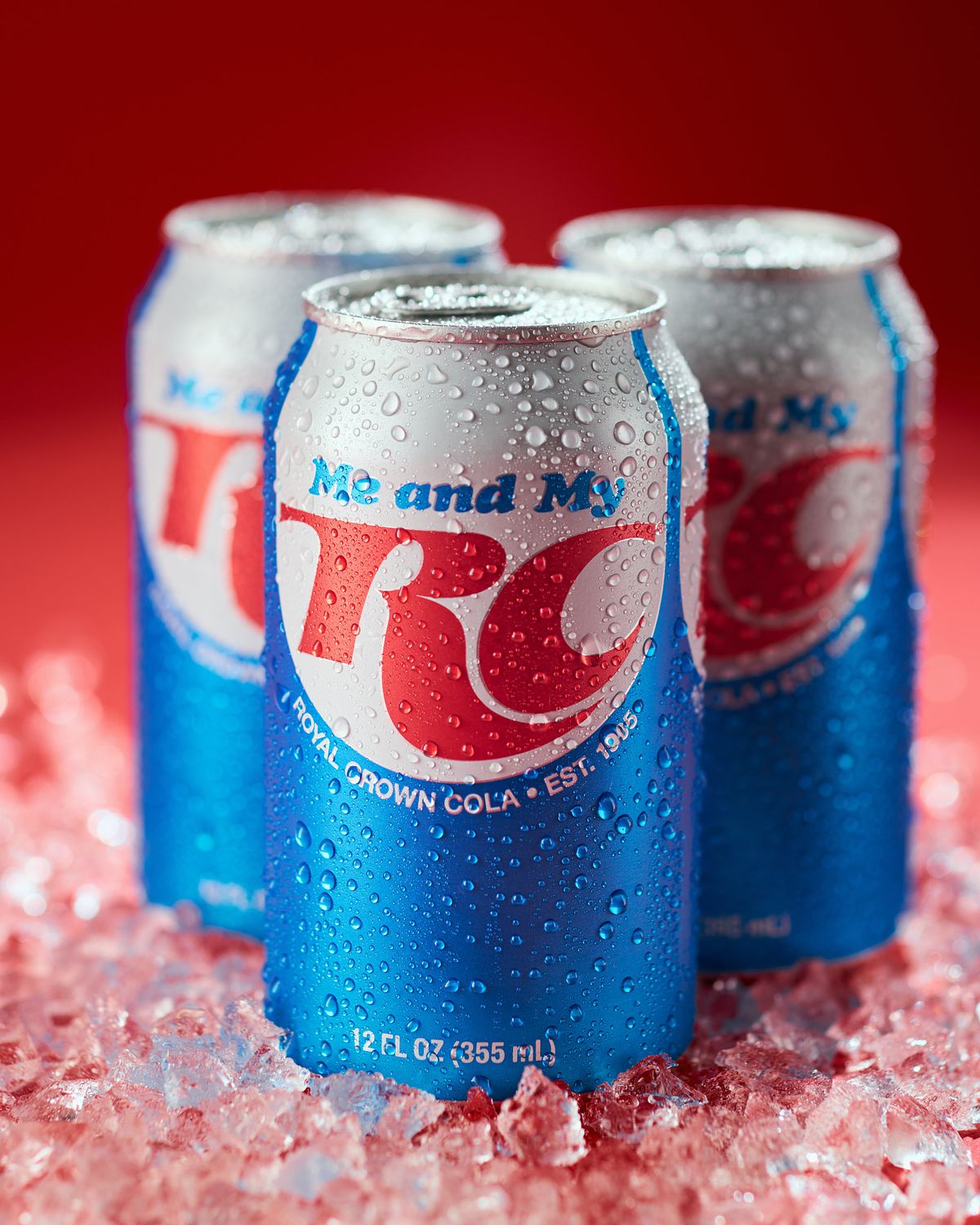 Three ice cold cans of a classic soda brand on a red background.