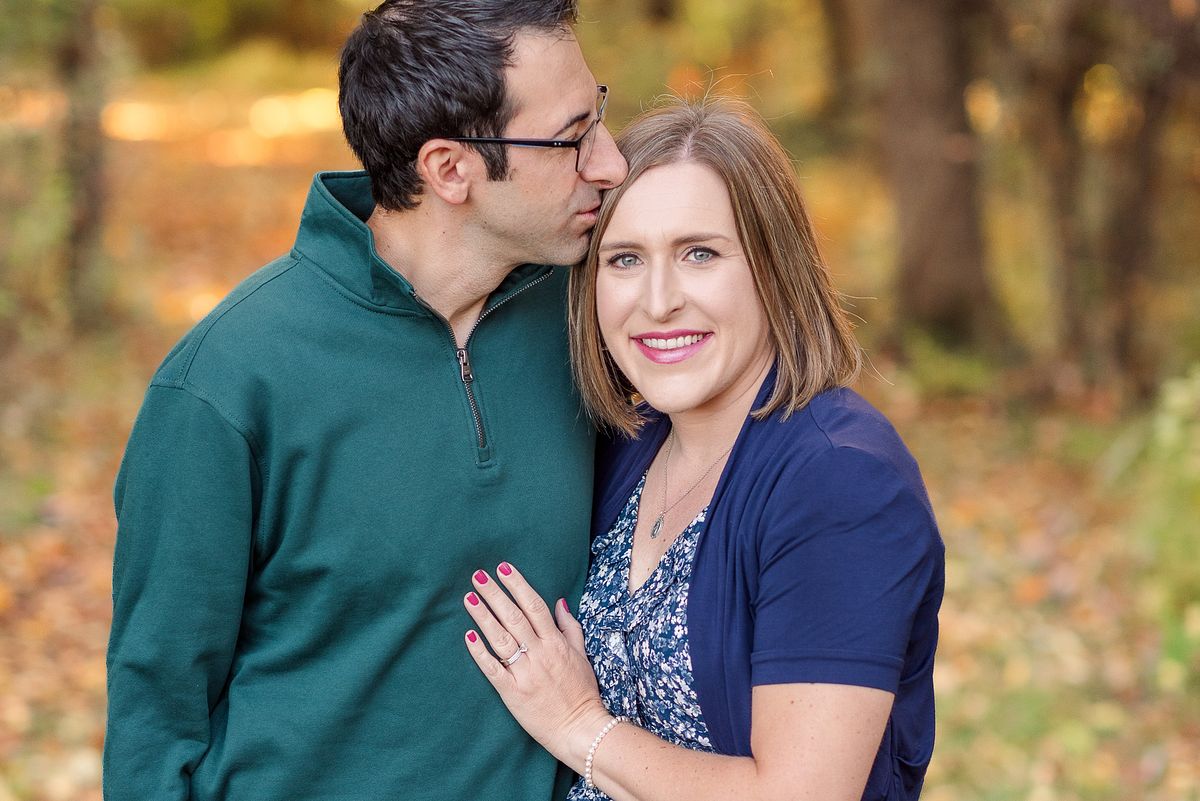 Husband kissing his wife on the forehead while she hugs him and smiles at the camera with a Cranberry Township, PA newborn photographer