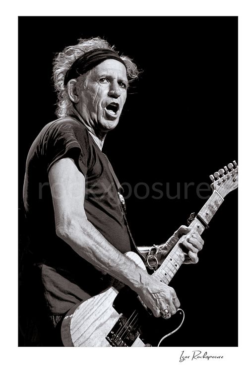 Vertical black and white image of Keith Richards of The Rolling Stones performing live with electric guitar in a close-up stage portrait