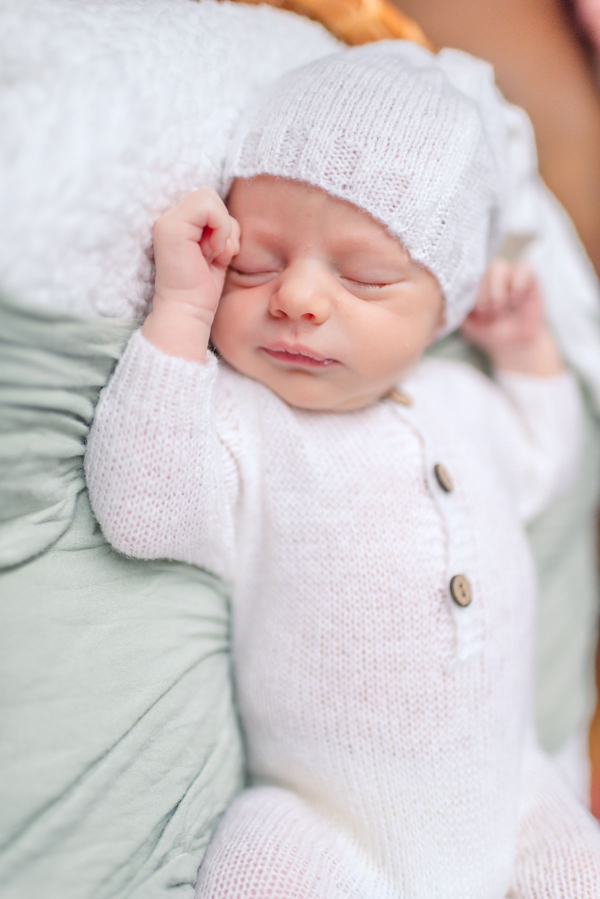 Baby boy in white pajama and hat lying on fluffy blanket and soft green accent piece