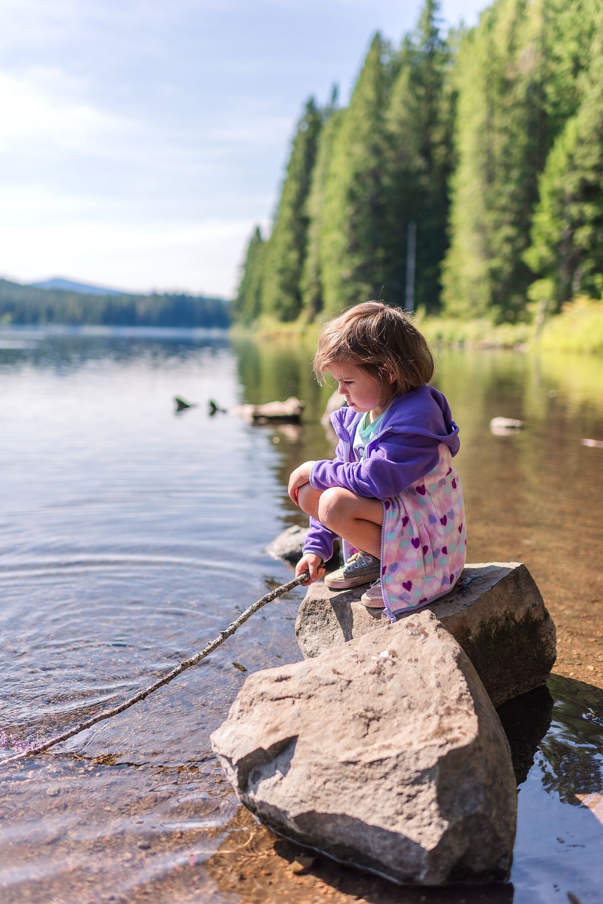 girl by the lake sitting on a large rock on road trip with cranberry twp, pa newborn photographer