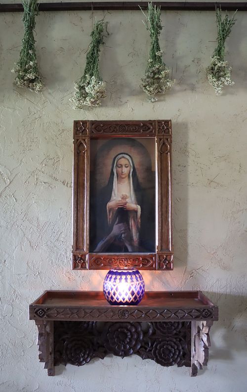 hand-carved shelf covered in roses and a gothic revival picture frame for a votive shrine in a Catholic home.