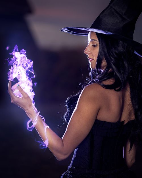 A witch observes purple flames encircling her arm.