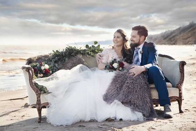 man and woman sitting on padded sofa beside sea