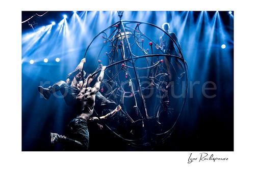 Horizontal color image of Pink with aerial acrobats on a suspended stage structure under bright blue concert beams