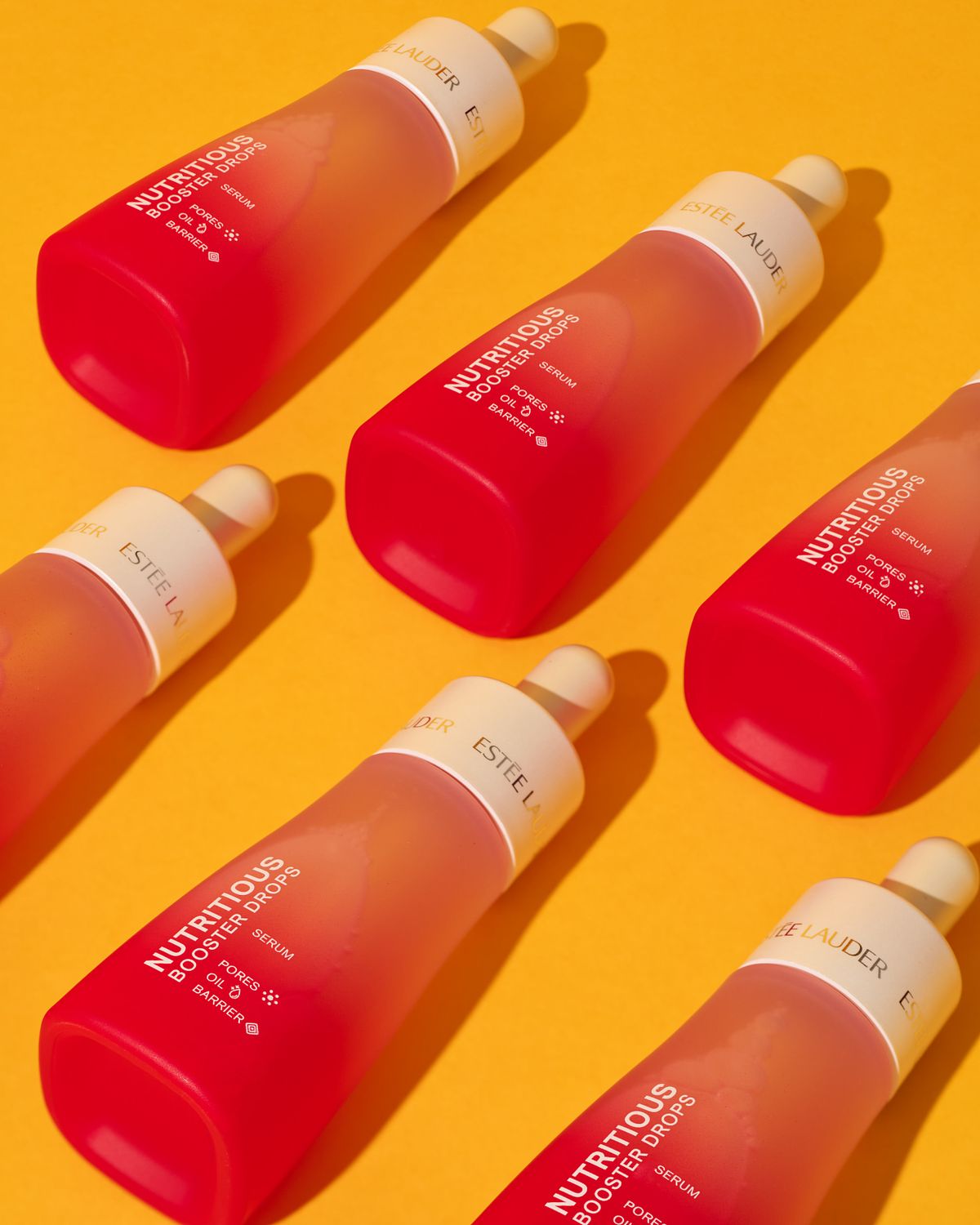 Six red cosmetics bottles laid in a pattern on a bright yellow surface.