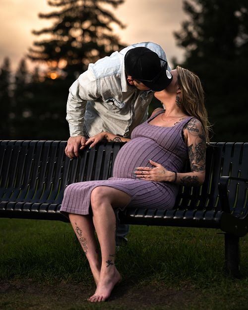 Expecting couple sharing a kiss in the park at sunset.