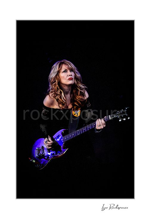 Vertical color image of Nancy Wilson performing with electric guitar during a Heart concert against a dark stage background