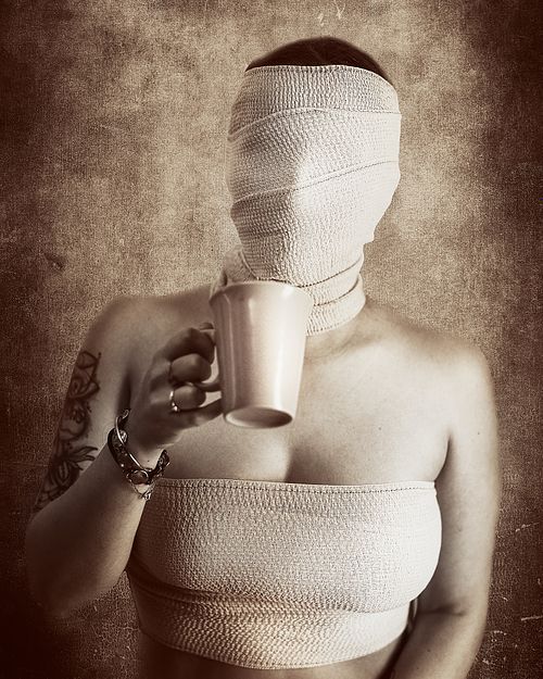 Portrait artistique d'une femme en bandages buvant une tasse de café, symbolisant la perte d'identité et la résilience silencieuse — photographie fine art Pascal Yennis, Namur, Belgique.