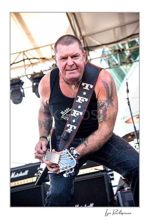 Vertical color image of an unidentified guitarist of Rose Tattoo playing guitar onstage in a tight outdoor live performance shot