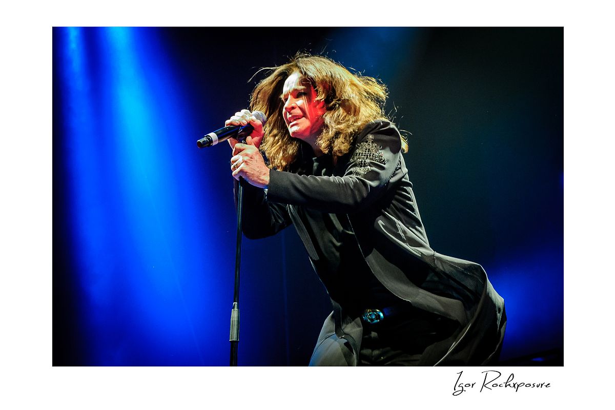 Ozzy Osbourne of Black Sabbath singing into a microphone during a live performance under dramatic blue stage lighting