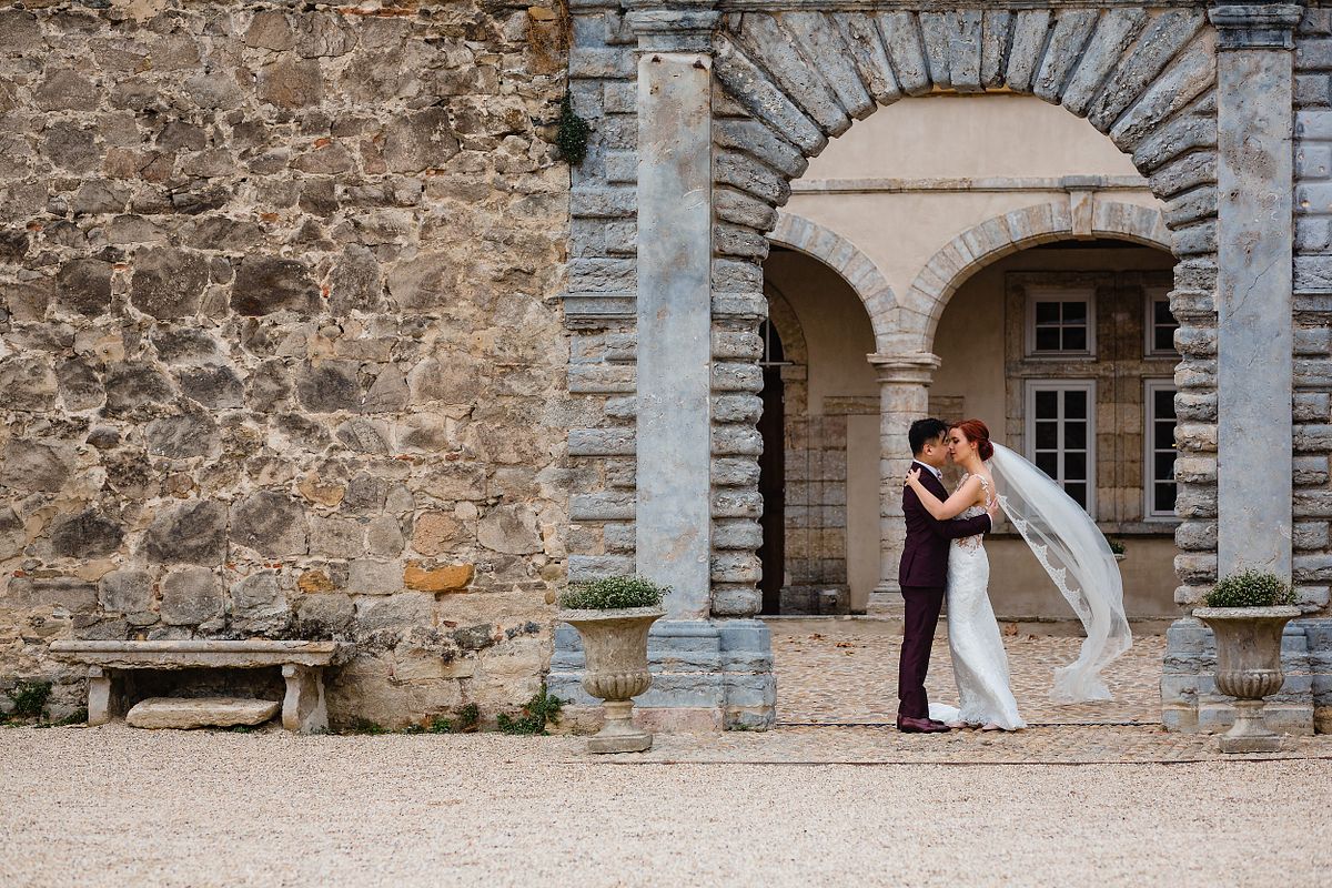 Tarif Photographe Mariage - Sebastien CLAVEL Photographe - Couple de mari&eacute;s s'embrassant sous un arc en pierre, &eacute;change romantique et &eacute;l&eacute;gant dans un d&eacute;cor historique