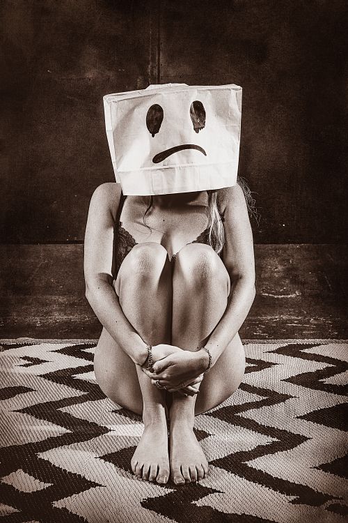 Femme assise au sol en lingerie avec un sac en papier sur la t&ecirc;te affichant un visage triste, illustrant l&rsquo;&eacute;puisement &eacute;motionnel et la solitude int&eacute;rieure malgr&eacute; une fa&ccedil;ade sociale