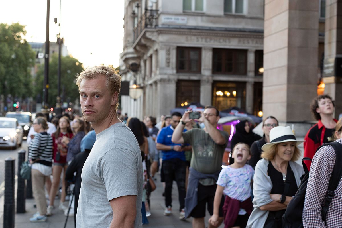 Man v&auml;nder sig mot kameran i en livlig London-gata med m&auml;nniskor i bakgrunden, redaktionellt milj&ouml;portr&auml;tt.