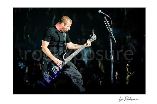 Horizontal color image of Mike Kroeger of Nickelback playing bass onstage beside a microphone stand during a live performance