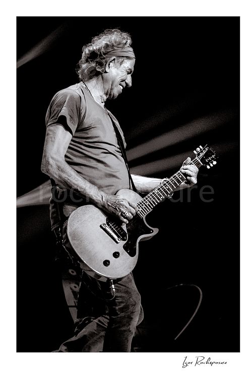 Vertical black and white image of Keith Richards of The Rolling Stones performing live with electric guitar in a close-up stage portrait
