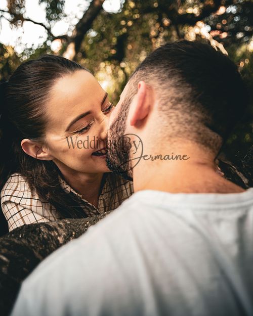 Close-up of Alex and Shelby sharing a kiss while reaching over a branch during their engagement shoot, captured by Weddings by Jermaine in a romantic and natural setting