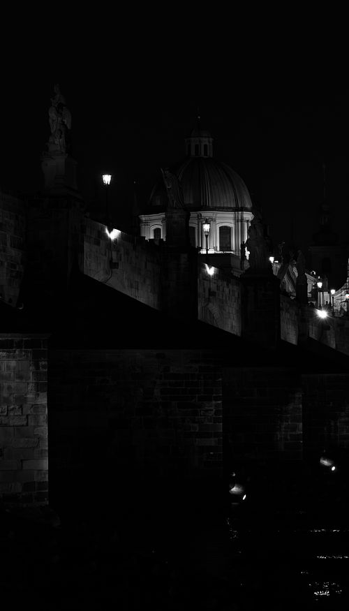 Les statues se découpent dans l’obscurité, guidant le regard vers le dôme éclairé. Une vision intime du pont Charles, entre silence et architecture.
