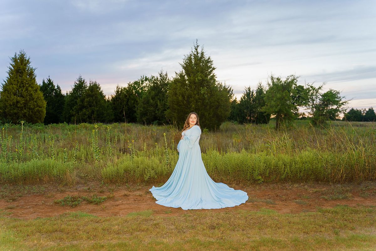 Pregnant woman posing in natural light with a flowing maternity gown.