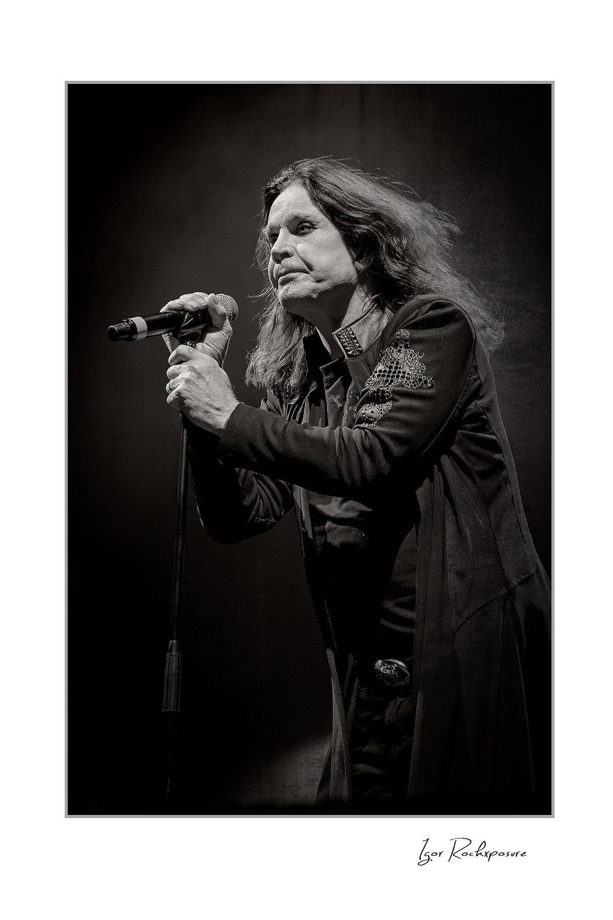 Ozzy Osbourne of Black Sabbath singing into a microphone captured in a dramatic black and white portrait during a live performance