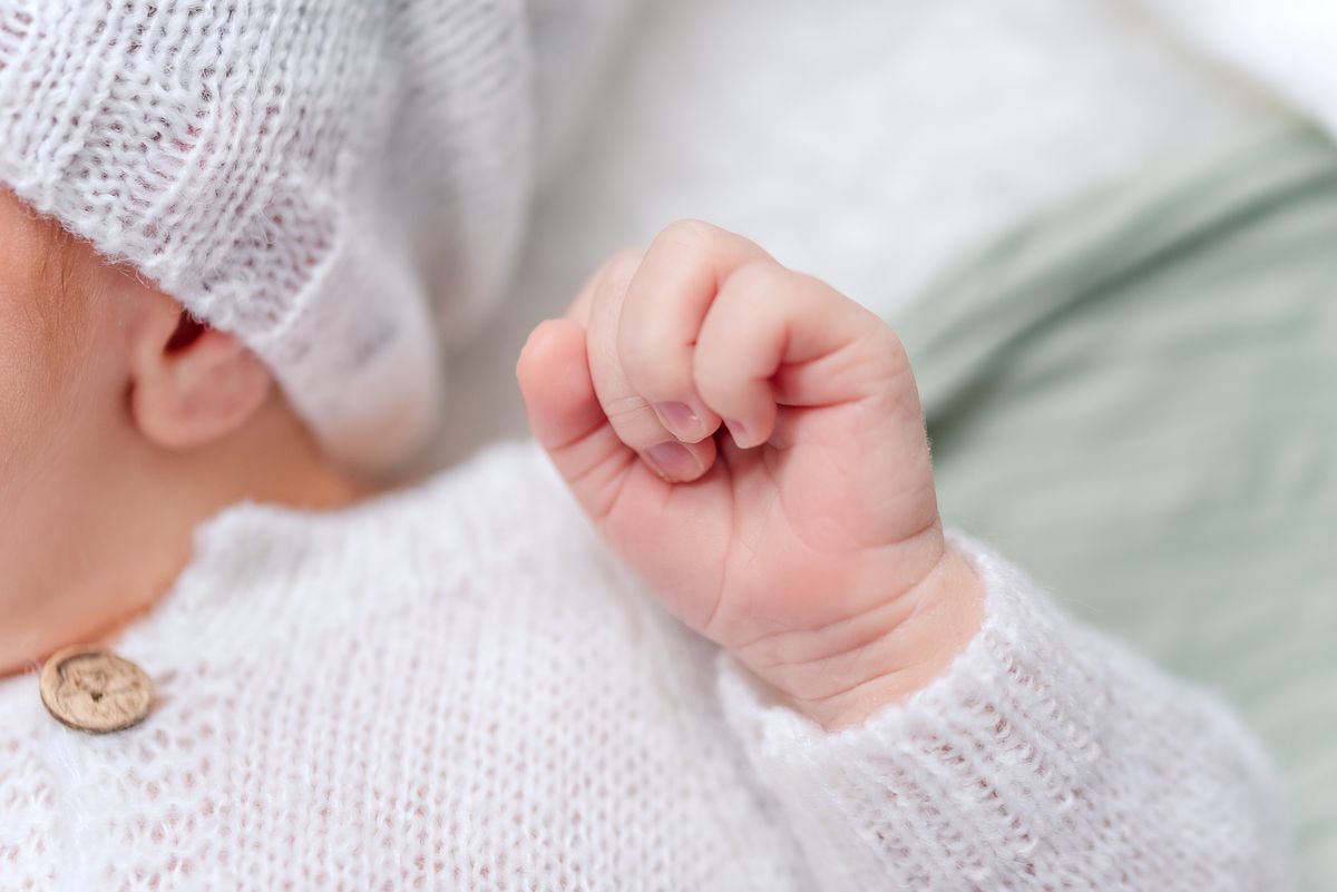 Baby hand details while baby boy sleeps in white pajamas and hat