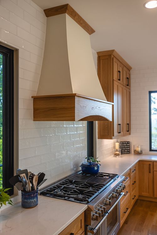 close up of gas range and hood with a seamless subway tile backsplash