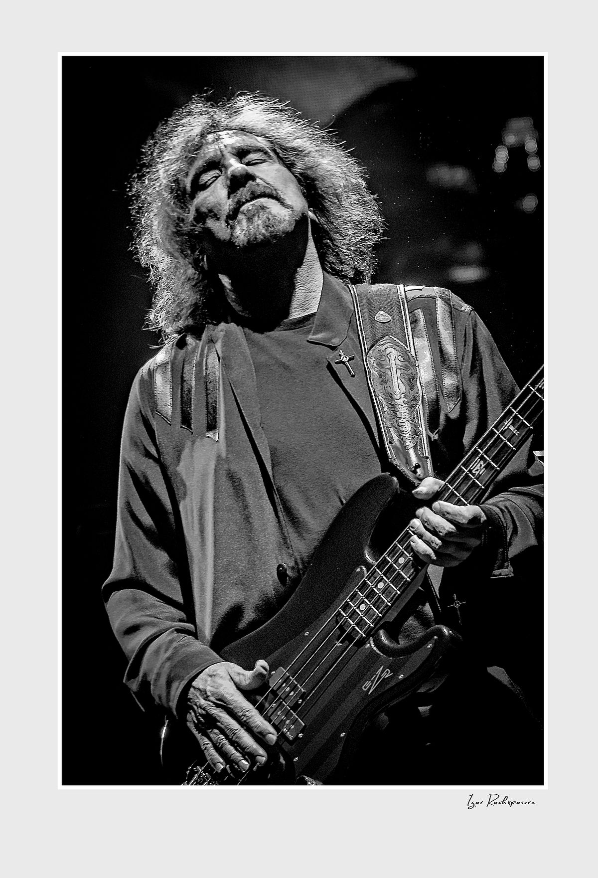 Black and white portrait of Geezer Butler of Black Sabbath playing bass guitar with head tilted back during a live performance