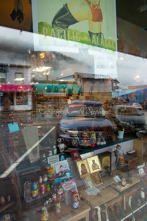 Seward, Alaska storefront featuring a 1930s retro poster, matryoshka dolls, Russian souvenirs, and fog-covered mountains in the background