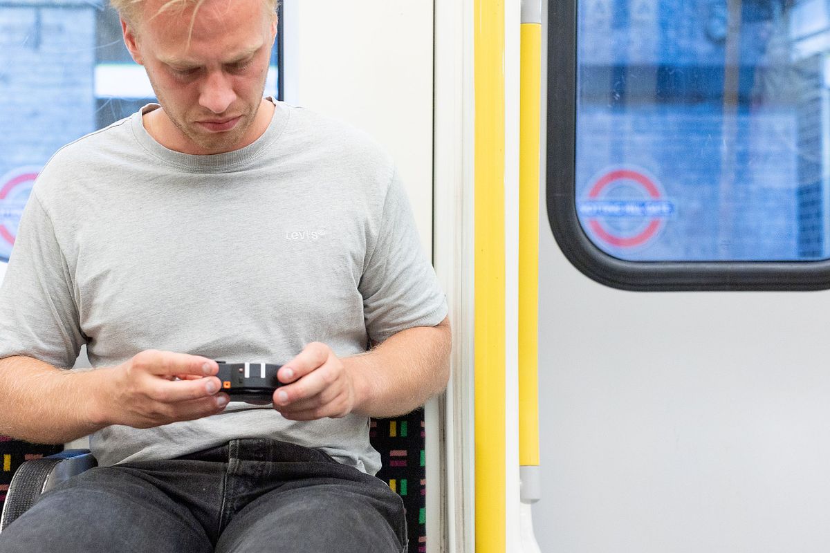 Man sitter i London Underground och tittar ner p&aring; en kamera, dokument&auml;rt portr&auml;ttmoment i kollektivtrafik.