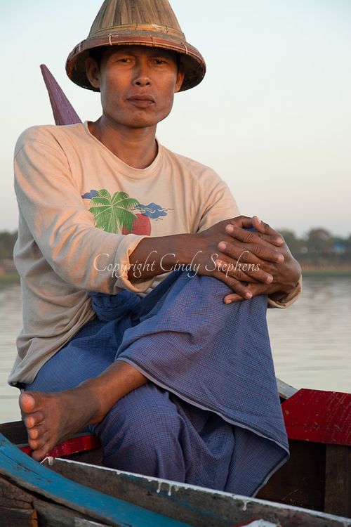Fisherman sitting cross-legged in a traditional wooden canoe on Inle Lake, Myanmar, showcasing local fishing culture.