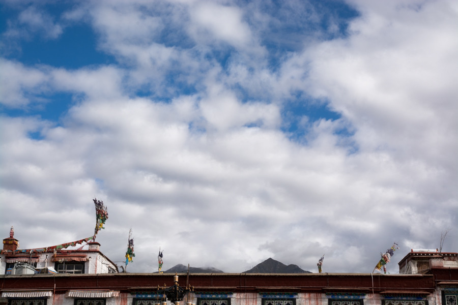 Blue skies and clouds with Tibetan prayer flags and building roof barely visible