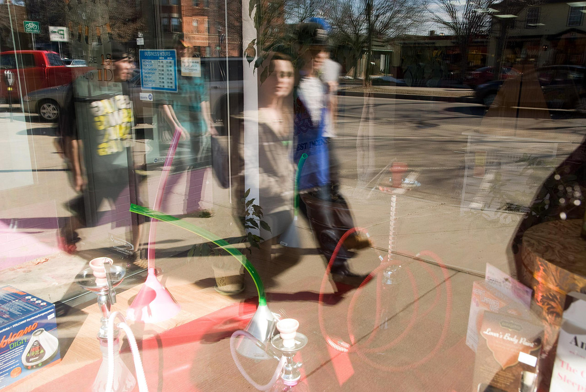 People walking on sidewalk in front of store selling hookah pipes