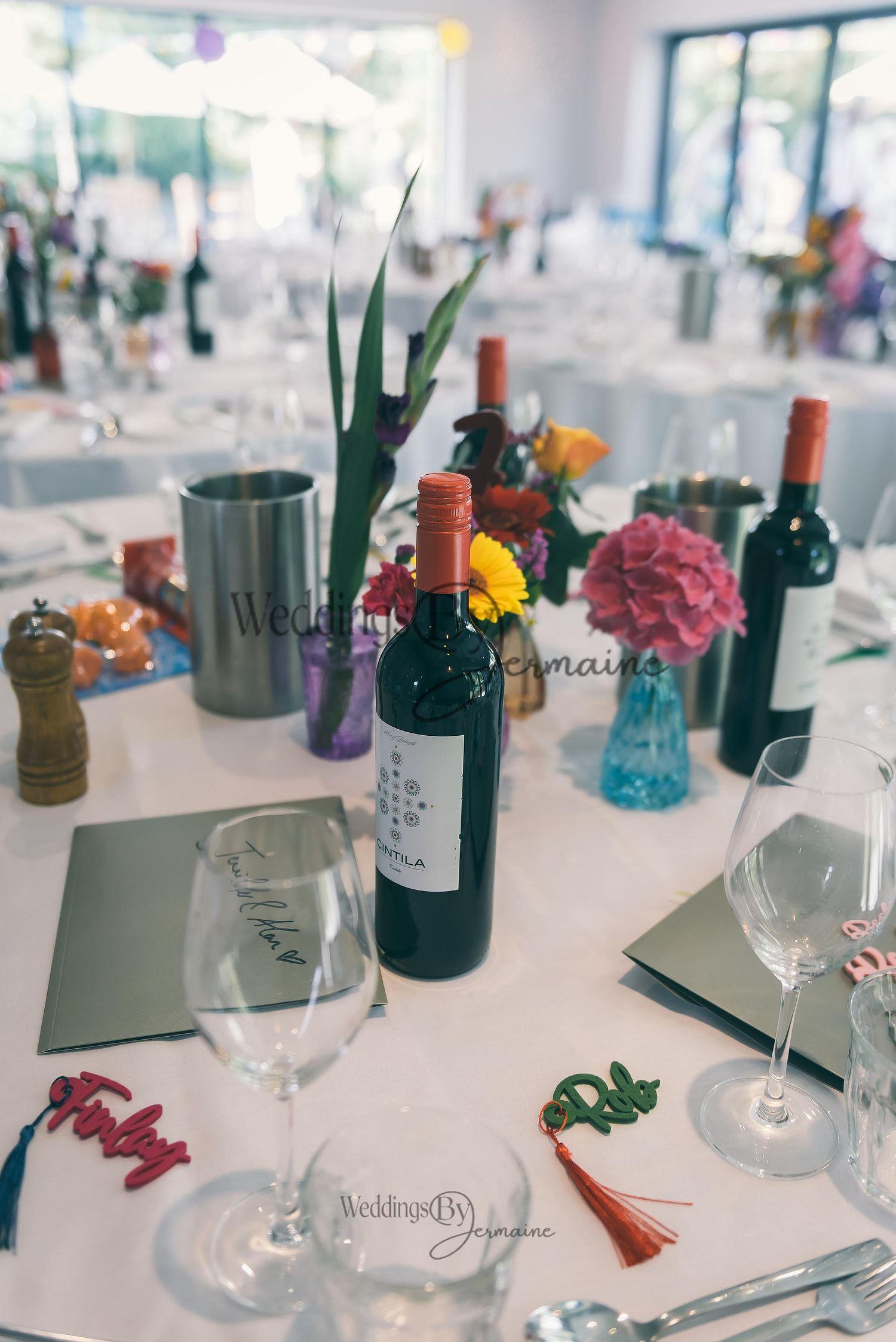 Wedding reception tables arranged with bottles of wine, cutlery, and personalized name tags, photographed by Weddings by Jermaine