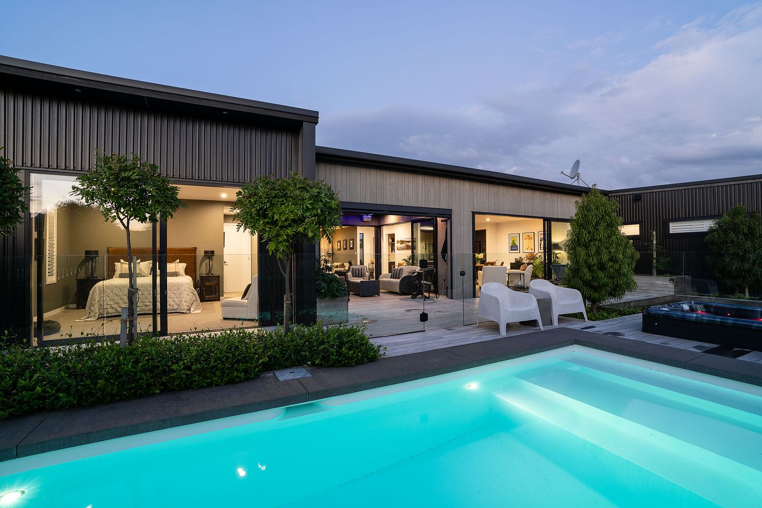 Luxury coastal home in Rangitahi, Raglan at sunset featuring architectural pool lighting and mountain views.