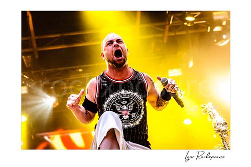 Horizontal color image of Ivan Moody of Five Finger Death Punch singing onstage with a microphone under intense yellow concert light