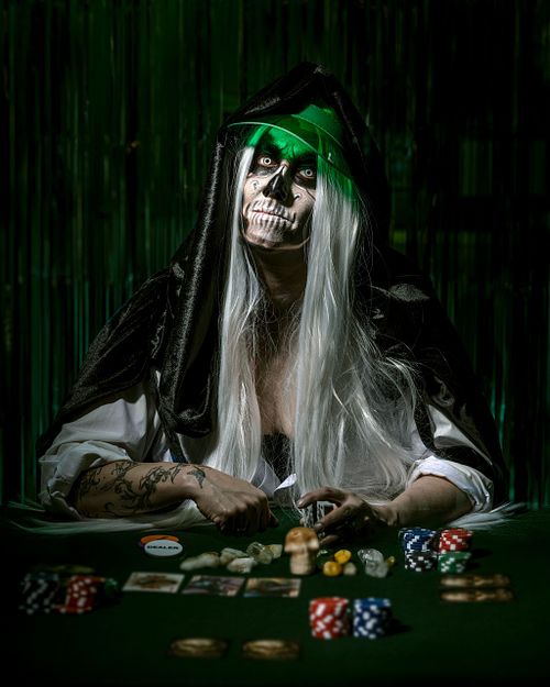 Female death with long white hair and dealer's green visor knocking on a poker table.